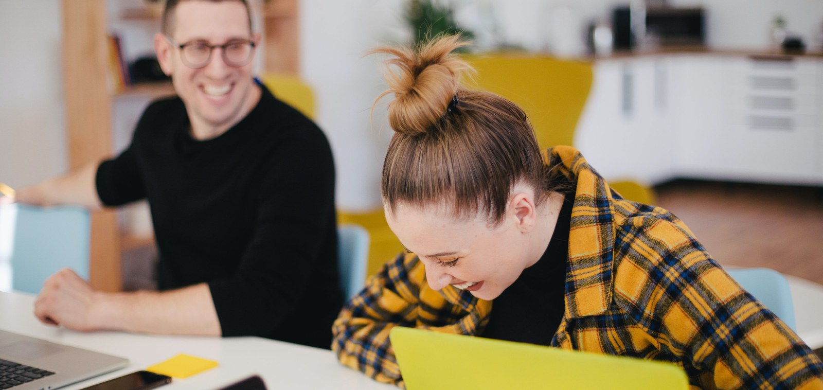 Young women and young men working in IT sitting in front of her laptops, laughing.